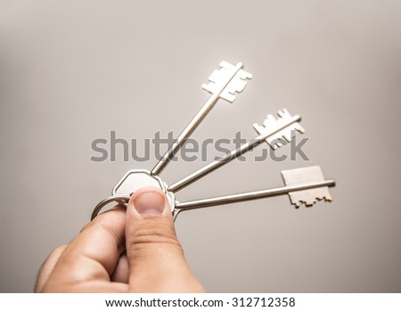Man's Hand with three big keys isolated on gray and white background. Hotspot on metal texture Empty space for inscription or objects 