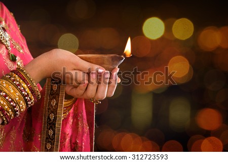 Close up Indian woman in traditional sari lighting oil lamp and celebrating Diwali or deepavali, fesitval of lights at temple. Female hands holding oil lamp, beautiful lights bokeh background. Royalty-Free Stock Photo #312723593