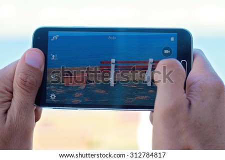 Close up on male hands taking photo of sea coast with mobile cell phone. Summer beach holiday vacation concept