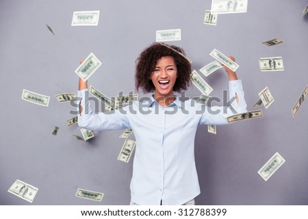 Concept photo of a cheerful afro american woman standing under rain with money on gray background