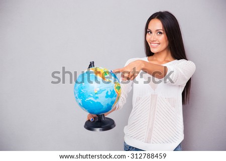 Portrait of a smiling young woman pointing finger at globe on gray background