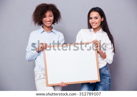 Portrait of a two girls holding blank board over gray background