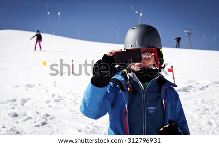 Woman taking photos with phone on ski slope - winter vacation