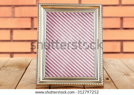 Old frame with striped canvas standing on table on brick wall background