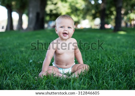 Happy baby with light and fluffy hair sitting on the grass and laughing. Summer and very warm. Happy smile.