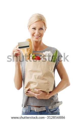 Portrait of smiling woman holding hand shopping paper bags full of food while other hand there is a credit card. Isolated on white background. 