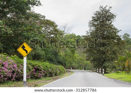 turning yellow traffic sign on road in countryside , nature background