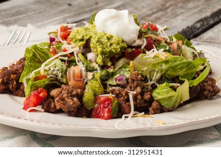 Taco salad on an antique platter on a weathered barn wood table freshly made