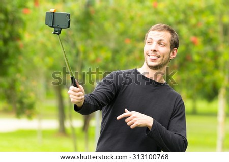 Hispanic man posing with selfie stick in park environment taking a photo of himself smiling.