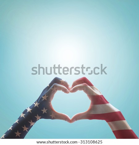 America flag pattern on people hands in heart shaped against blue sky background