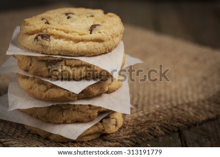 Stack of chewy chocolate chip cookies, fresh from the oven. Sat on a hessian and wood surface. Each cookie is separated by an sheet of grease proof paper Royalty-Free Stock Photo #313191779