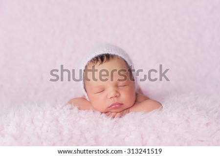 Portrait of nine day old sleeping newborn baby girl. She is wearing a knitted bonnet and is lying on a soft, fuzzy, pink blanket.