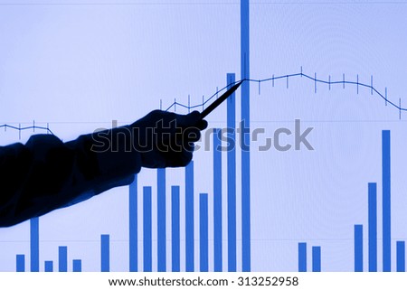 Silhouette of a man's arm pointing to a rising graph on an LCD display. Focus is on the LCD display.
