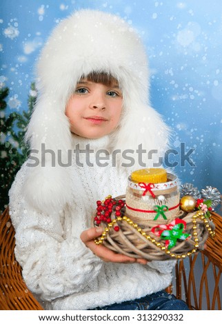 beautiful girl in a white cap and knit sweater holding a candle on the background of Christmas decorations