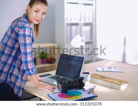 Female photographer standing near desk with laptop