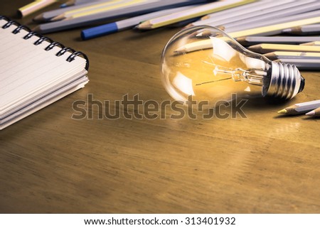 Glowing light bulb with pencils and notebook on wood table