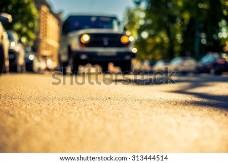 Clear day in the big city, a car rides through the streets near the park. View from the level of asphalt, image in the yellow-blue toning