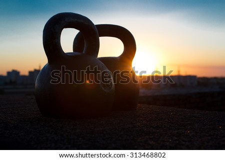 Close-up shot of two 16-kilogram cast iron kettlebell over sunset sky background. Sports equipments. Concept of healthy lifestyle and physical activity. Dramatic dark shot