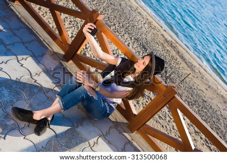 Hipster girl making self portrait with her smart phone digital camera while enjoying summer day outdoors, female in fashionable clothes posing while photographing herself for social network picture