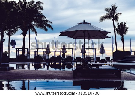 Silhouette palm tree with umbrella and chair in the luxury hotel pool resort at sunrise times - Vintage filter processing style pictures