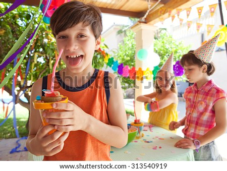 Portrait of boy child at a home garden birthday party drinking fruit juice with a straw with colorful decorations, outdoors. Kids having fun and enjoying a party together on holiday, sunny exterior.