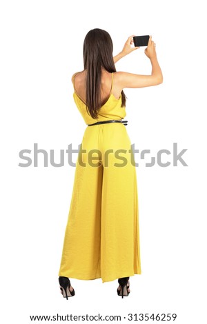Rear view of young elegant woman taking photo with smartphone. Full body length portrait isolated over white studio background. 