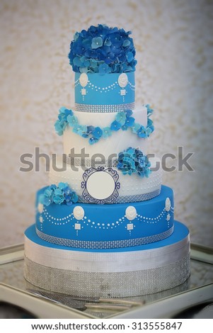 One large beautiful delicious many-tier decorated wedding cake white and blue colours with flower garlad and hydrangea bouquet on top, vertical picture