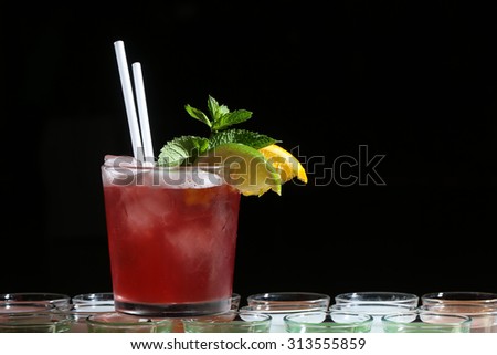 One alcoholic long red cocktail in drinking glass with straws mint leaf ice cubes green lime and yellow lemon slices standing on goblets on black studio background copyspace, horizontal picture