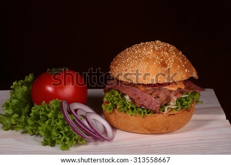 Big tasty appetizing fresh burger of green lettuce red tomato cheese bacon slice meat cutlet violet oinion and white bread bun with sesame seeds on black backgeound closeup closeup, horizontal picture