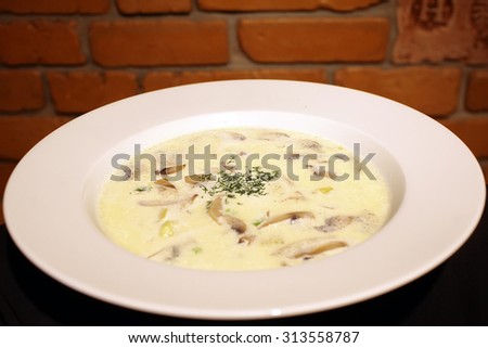 Delicious classical sheese cream soup with sliced mushrooms and greeny in white round plate close up, horizontal picture