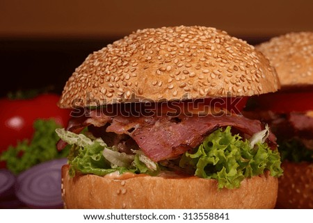 One big tasty appetizing fresh burger of green lettuce red tomato cheese bacon slice violet oinion and white bread bun with sesame seeds closeup, horizontal picture