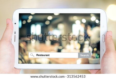 Hand holding tablet with restaurant word on search bar over blurred restaurant background, restaurant reservation, food online, food delivery concept