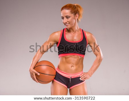Beautiful muscular woman is holding a basket ball, standing on grey background.