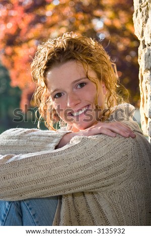 Senior Portrait of redhead female high school student with fall foliage in the background.