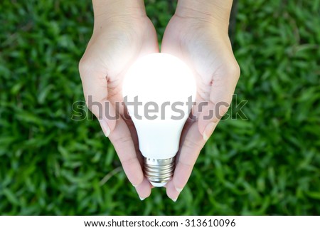 LED bulb with lighting in the human hand with green grass background Royalty-Free Stock Photo #313610096