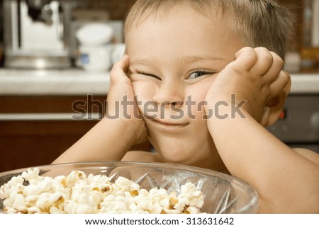 Baby boy is posing a face near the  bowl of popcorn on a kitchen equipment background