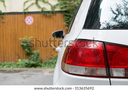 White car parked in front of a garage. In the background forbidden parking sign. Focus on car tail light.
