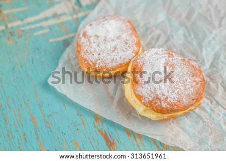 Sweet sugary donuts on rustic wooden kitchen table, tasty bakery on crumpled baking paper in vintage retro toned image