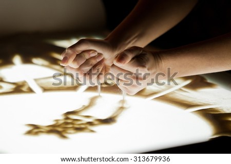 Sand animation.The girl's arms, drawing sand in dark colors