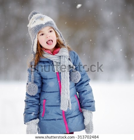 Funny little girl catching snowflakes with her tongue in beautiful winter park during snowfall