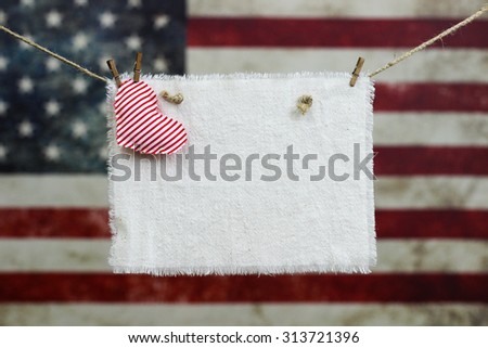 Muslin sign with red heart hanging in front of blurred background of vintage American flag on canvas