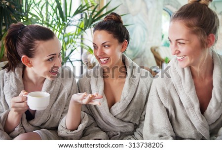 Three young happy women drinking tea at spa resort Royalty-Free Stock Photo #313738205