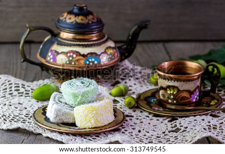 Traditional Turkish coffee set: painted copper teapot with cup, Turkish delight on a plate and acorns on old wooden background