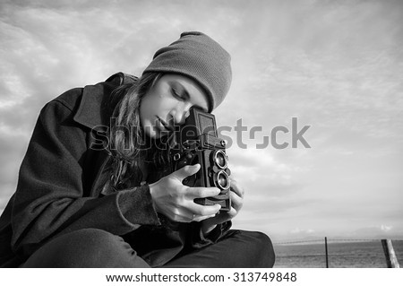 Young Female Photographer Taking Ocean Scenery Using Vintage Camera. Lifestyle Portrait Captured in Monochrome Color.