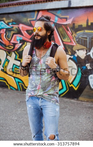 young guy with a beard wearing sunglasses and headphones listening to music on the street