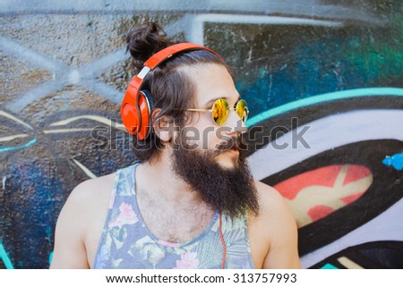 Travel photo of hipster young man posing on the city street with bag pack,travel bag,adventure concept.Stylish young beard man relaxed at sunny day on the park.New York city line.Earphones
