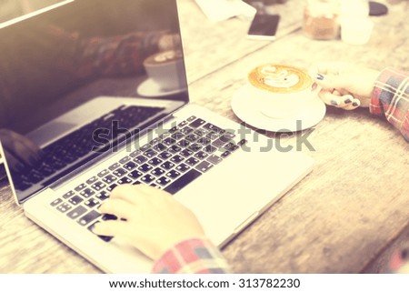 Girl hands with laptop and cappuccino on a wooden table, vintage photo effect