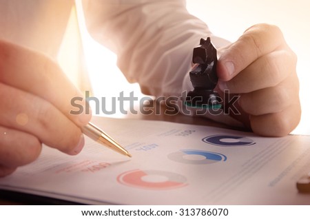 Closeup of businessman working with document graph and holding a chess piece.