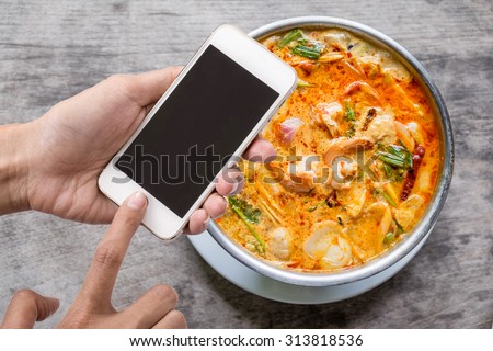 Woman holding smartphone against Tom Yum Goong on table or mobile phone with blank mobile.Shallow depth of field.