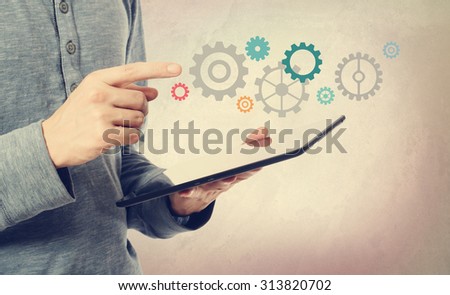 Young man pointing at colorful gears over a tablet computer